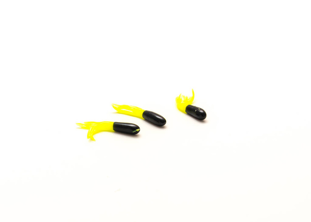 Trzy świecące mini przynęty ogonowe w kolorze czarnym i żółtym Chartreuse izolowane na białym tle. Świecące miękkie przynęty Robaki Jig Tails Light. - Zdjęcie, obraz