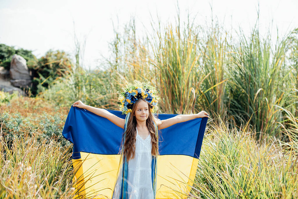 Ukrainian child girl in embroidered shirt vyshyvanka with yellow and blue flag of Ukraine in field. - Φωτογραφία, εικόνα