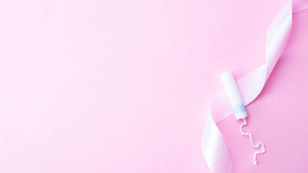 Tampon woman feminine hygiene. Pink ribbon with menstrual tampon on pink background. Menstruation feminine period. Soft tender protection for women critical days - Zdjęcie, obraz