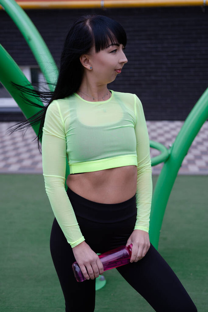 sporty woman in black and green sportswear doing sport exercises outside on sport playground. perfect healthy slim body - Fotografie, Obrázek