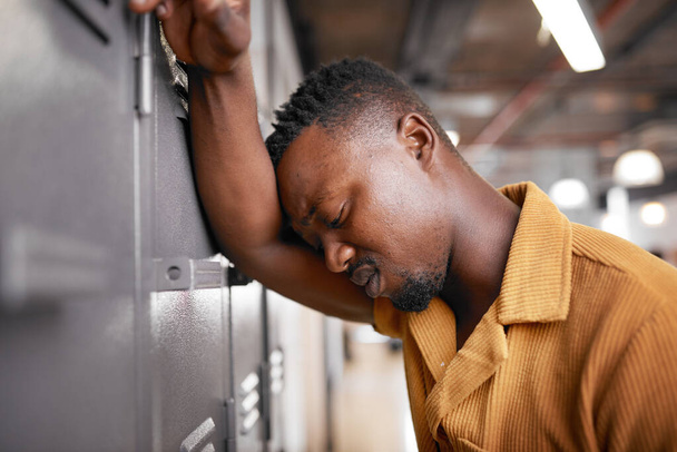 A young black man leans against the campus locker looking upset at college - Photo, image