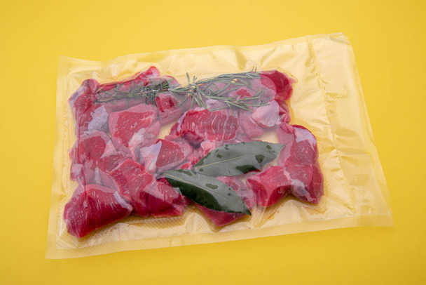 Çiğ sığır eti yahnisi, bir parça çiğ et, vakum paketlenmiş, sarı arka planda izole edilmiş soous vide pişirme için kapatılmış. - Fotoğraf, Görsel