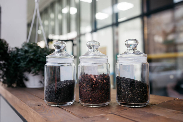 Loose tea in glass jars. Green tea with hibiscus and wild rose, chamomile in glass jars on table. - Fotó, kép
