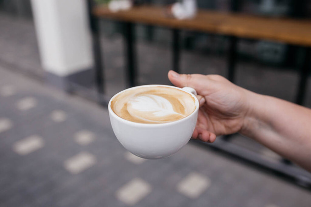 Frau mit Latte-Art-Kaffee auf Holztisch im Café. Kaffee im Becher. - Foto, Bild