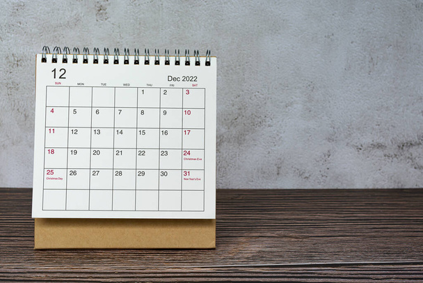 Diciembre 2022 calendario blanco en escritorio de madera. Fecha de celebración y espacio de copia. - Foto, imagen