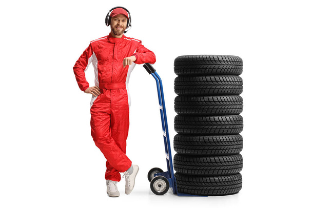 Full length portrait of a race team member leaning on a hand truck with tires isolated on white background - 写真・画像