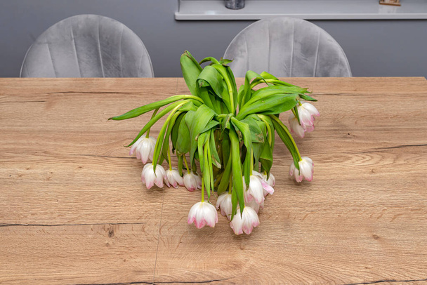 Egy csokor hervadt lila tulipán áll egy vázában az asztalon.. - Fotó, kép