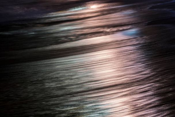 Unawatuna, Sri Lanka Captura abstracta de una ola en la noche con reflejos de la luz de la ciudad. - Foto, Imagen