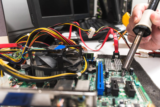 IT technician soldering a part of a computer motherboard in an office - Photo, image