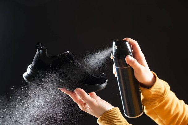 Uma mulher aplica um spray de um cilindro com um líquido repelente de água às migalhas das crianças. Cuidado com sapatos, eliminação de odor desagradável. - Foto, Imagem