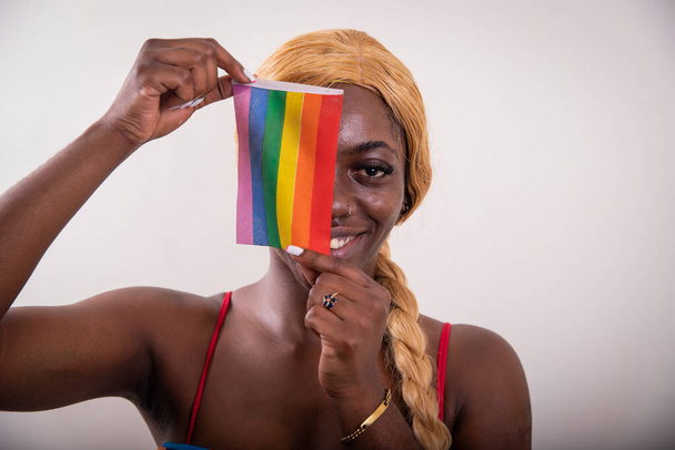 Retrato de estudio de una chica lesbiana posando con la bandera del arco iris cubriendo la mitad de su cara - Foto, Imagen