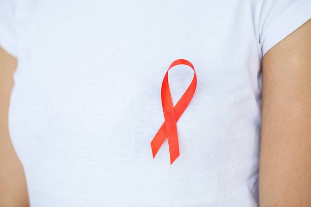Γυναίκα χέρι κρατώντας κόκκινη κορδέλα HIV, παγκόσμια ημέρα του AIDS κορδέλα ευαισθητοποίησης. - Φωτογραφία, εικόνα