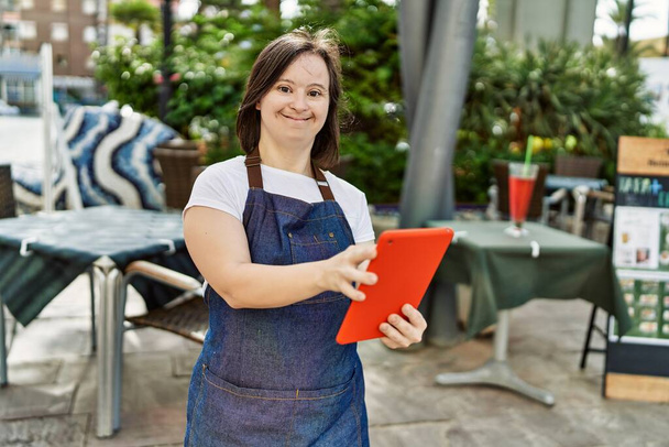 Jovem mulher síndrome de down usando avental usando touchpad no terraço da cafetaria - Foto, Imagem