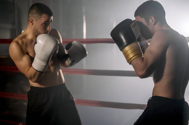 Two professional young muscular shirtless male boxers fighting in a boxing ring. - Fotó, kép