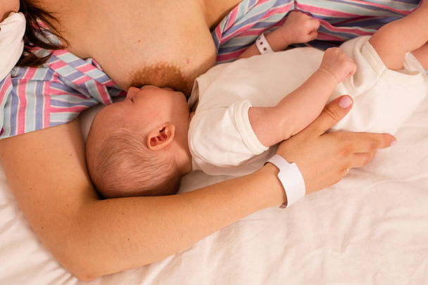 The mom is breastfeeding her newborn baby on the bed - Foto, Imagen