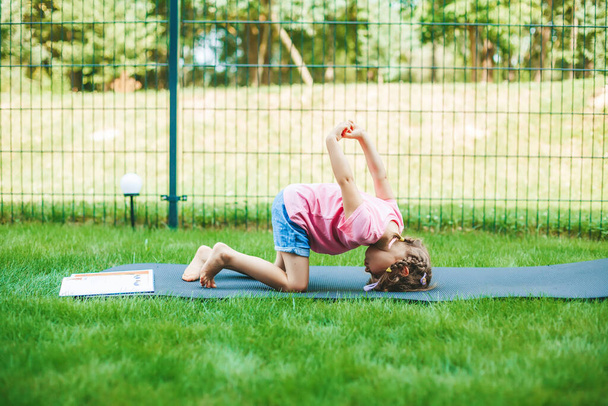 Little girl stretching on the roll mat practicing yoga outdoors. Yoga for children. Kid's healthy lifestyle. - Фото, изображение