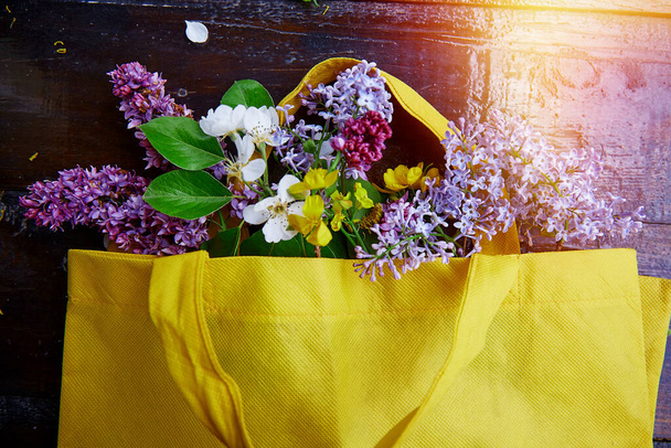 Voorjaarsboeket van lelies, abrikozenbloesems, bloemen in een gele zak. Duurzame, cottage core, verbinden met natuurconcept. - Foto, afbeelding