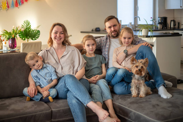 rodinný portrét. rodinná fotka, na které se máma, táta, dcery, syn a pes usmívají a objímají na gauči v útulné atmosféře - Fotografie, Obrázek