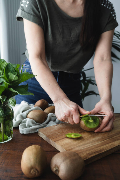 Una donna in cucina che affetta kiwi. Ragazza preparare frutta fresca e succosa - Foto, immagini
