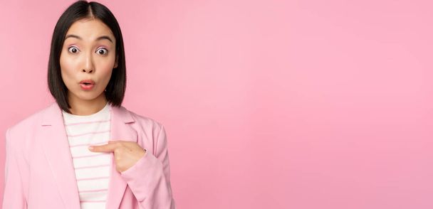 アジアの実業家の肖像画は、ピンクの背景に訴訟を提起し、顔に不信感で自分自身を指して、驚いて反応します - 写真・画像