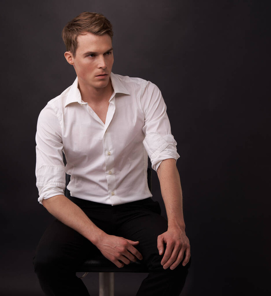 Awaiting his lady. A handsome young man sitting in formal clothes against a black background. - Foto, imagen
