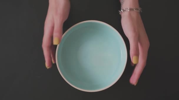 Sarı manikürlü kadınların elleri siyah arkaplanda mavi bir tabağı düzeltir - Video, Çekim