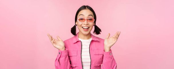 Imagen de chica asiática mirando sorprendida y emocionada, sonriente, reacción asombrada a las grandes noticias, de pie sobre fondo rosa - Foto, imagen