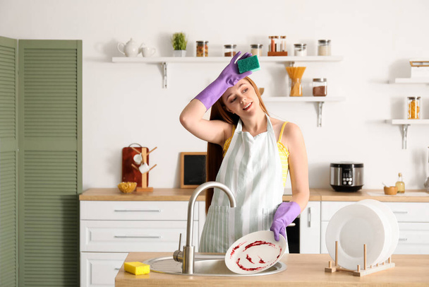 Κουρασμένη νεαρή γυναίκα πλένει πιάτα στο σπίτι - Φωτογραφία, εικόνα