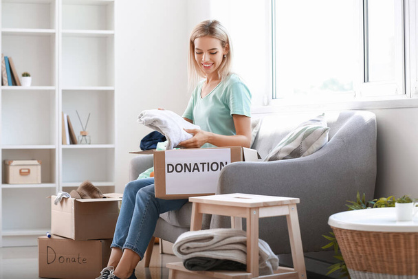 Junge Frau legt Kleidungsstücke für Spende zu Hause in Box - Foto, Bild
