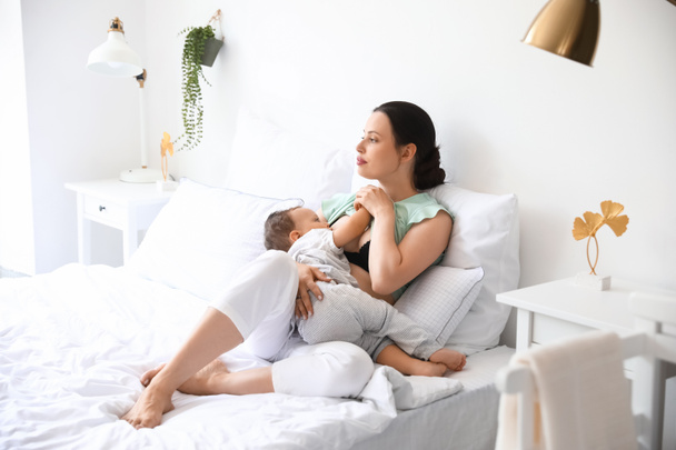 mooie jonge moeder borstvoeding haar schattige baby op bed - Foto, afbeelding