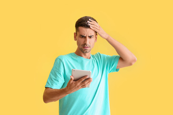 Беспокойный молодой человек с планшетом на цветном фоне - Фото, изображение