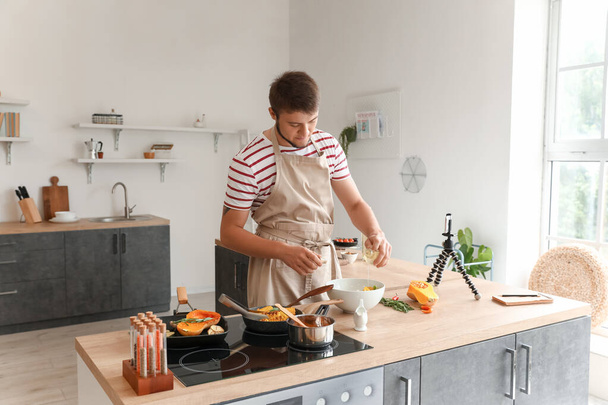 Junger Mann gießt in Küche Öl in Schüssel mit Salat - Foto, Bild