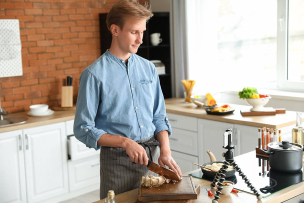Young man cutting mushrooms while following cooking video tutorial in kitchen - Photo, Image