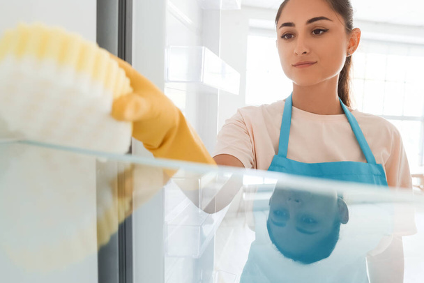 Fiatal nő takarítás hűtőszekrény a konyhában - Fotó, kép