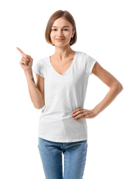 Beautiful young woman in stylish t-shirt pointing at something on white background - Foto, Imagem