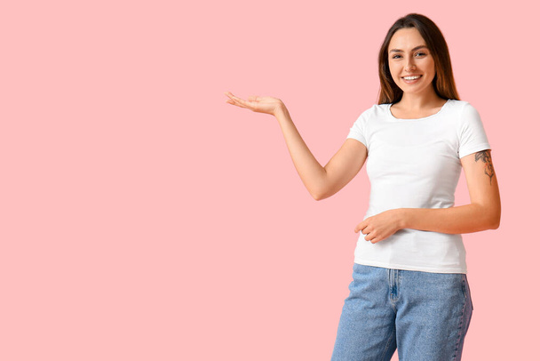 Mujer joven en camiseta en blanco mostrando algo en el fondo de color - Foto, Imagen