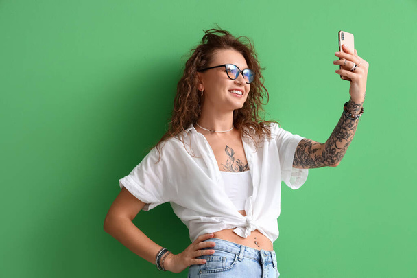 Hermosa mujer tatuada tomando selfie sobre fondo verde - Foto, Imagen
