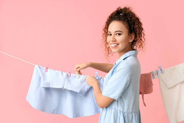 jong Afro-Amerikaanse vrouw opknoping schoon rok met wasknijper op roze achtergrond - Foto, afbeelding