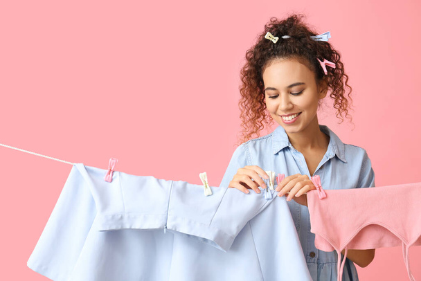 Young African-American woman hanging clean skirt with clothespin on pink background - Φωτογραφία, εικόνα