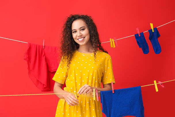 Young African-American woman hanging clothespin on red background - Foto, Bild