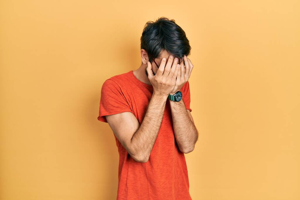 Young hispanic man wearing casual clothes and glasses with sad expression covering face with hands while crying. depression concept.  - Photo, Image