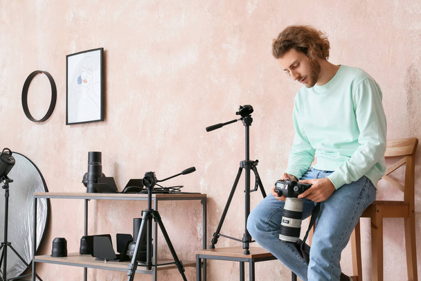 Άνδρας φωτογράφος με κάμερα κάθεται σε καρέκλα κοντά σε ροζ τοίχο στο σύγχρονο στούντιο - Φωτογραφία, εικόνα