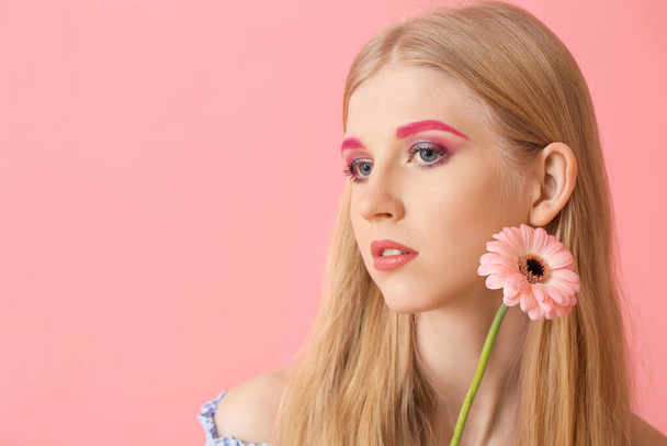 Woman with creative makeup and gerbera flower looking aside on color background - Foto, Imagen