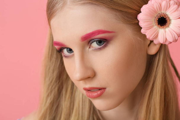 Young woman with creative makeup and gerbera flower on color background - Photo, Image
