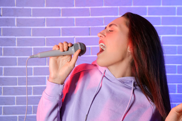 Renkli tuğla arka planda şarkı söyleyen havalı genç bir kadın. - Fotoğraf, Görsel