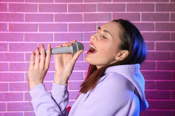 Cool young woman singing on color brick background - Photo, Image