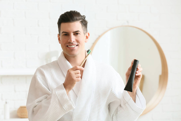 Handsome young man with activated charcoal tooth paste and brush in bathroom - Photo, Image