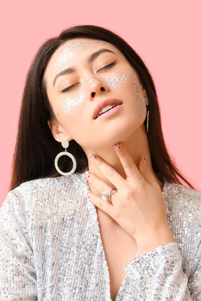 Asian woman with glitter makeup touching neck on color background - Fotografie, Obrázek