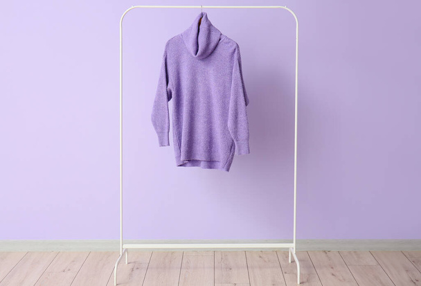 Rack met lila trui in de buurt van kleur muur - Foto, afbeelding