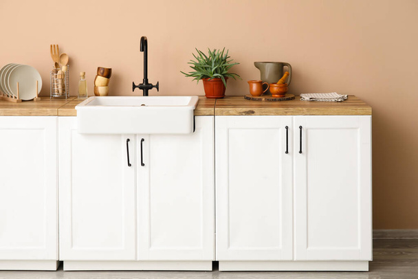 Liczniki z umywalką, przyborami domowymi i kuchennymi w pobliżu beżowej ściany - Zdjęcie, obraz